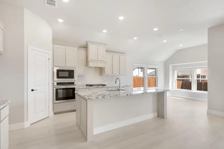 Open kitchen with white cabinets, granite island, stainless steel appliances, and light wood floors