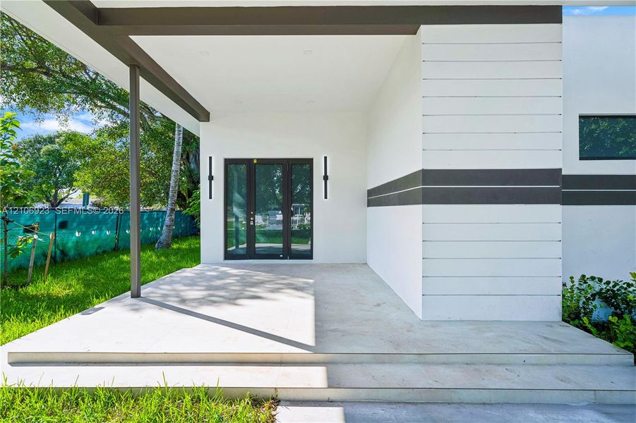 Modern entrance featuring horizontal wood-panel siding, a covered concrete porch, tiered stairs, and dual vertical wall-mounted exterior light fixtures Modern entrance featuring horizontal wood-panel siding, a covered concrete porch, tiered stairs, and dual vertical wall-mounted exterior light fixtures