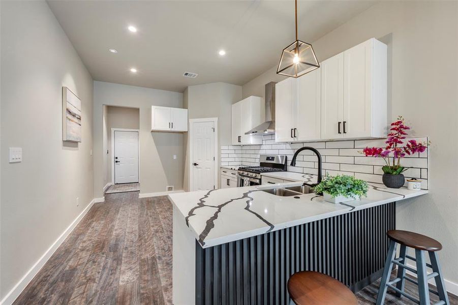 Kitchen featuring a kitchen breakfast bar, stainless steel gas stove, tasteful backsplash, white cabinetry, and dark wood-type flooring