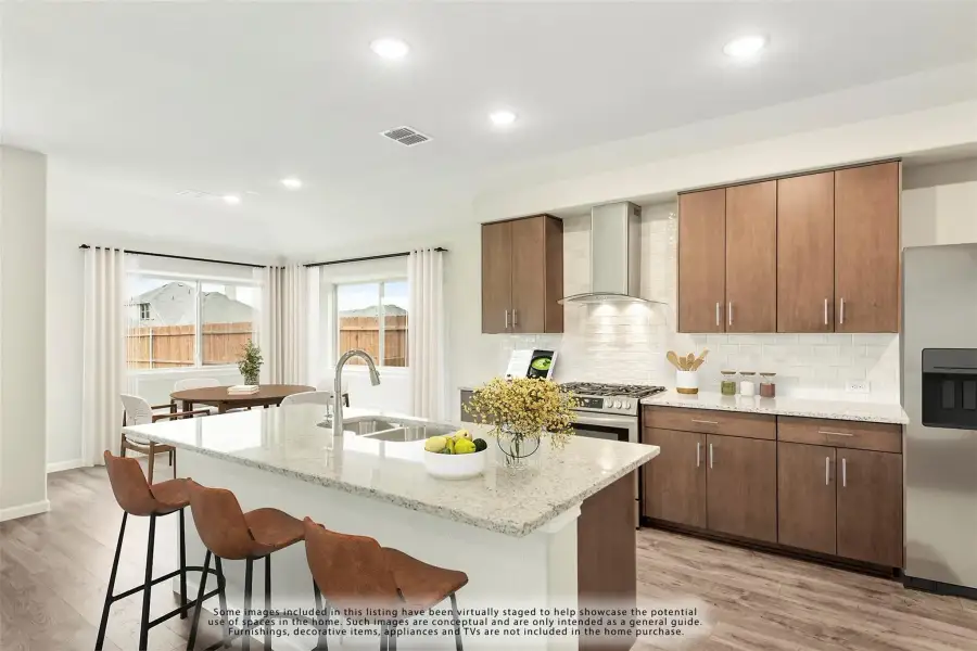 Kitchen with granite island, brown cabinets, subway tile backsplash, and stainless steel range with hood vent