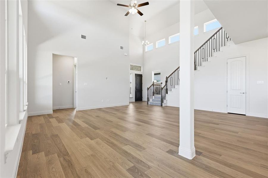 Unfurnished living room featuring light wood-style floors, a ceiling fan, and a high ceiling