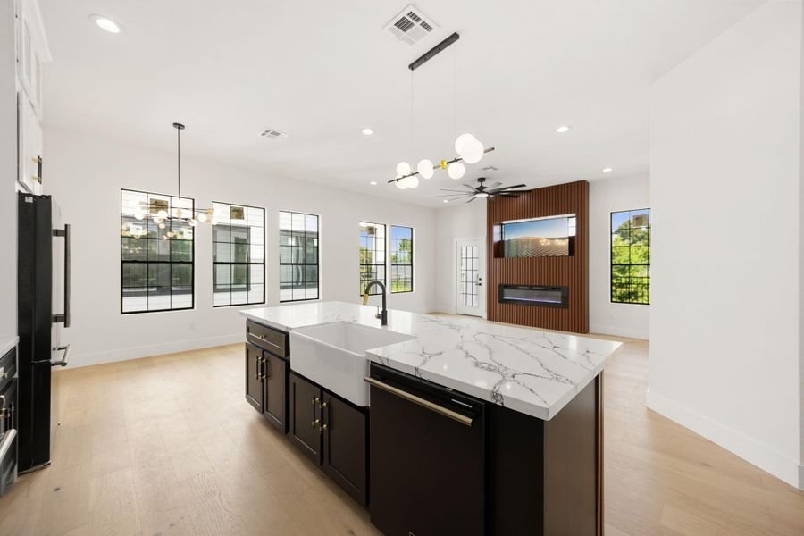 The kitchen features a beautiful farmhouse sink, dishwasher, premium appliances, and a breakfast bar overlooking the living area. From here, you can also enjoy views of the balcony and the striking retractable TV with an electric fireplace, creating a stylish focal point for the space.