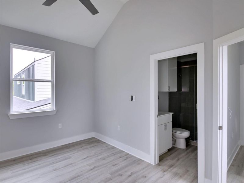 Unfurnished bedroom with lofted ceiling, light wood-type flooring, a ceiling fan, and connected bathroom