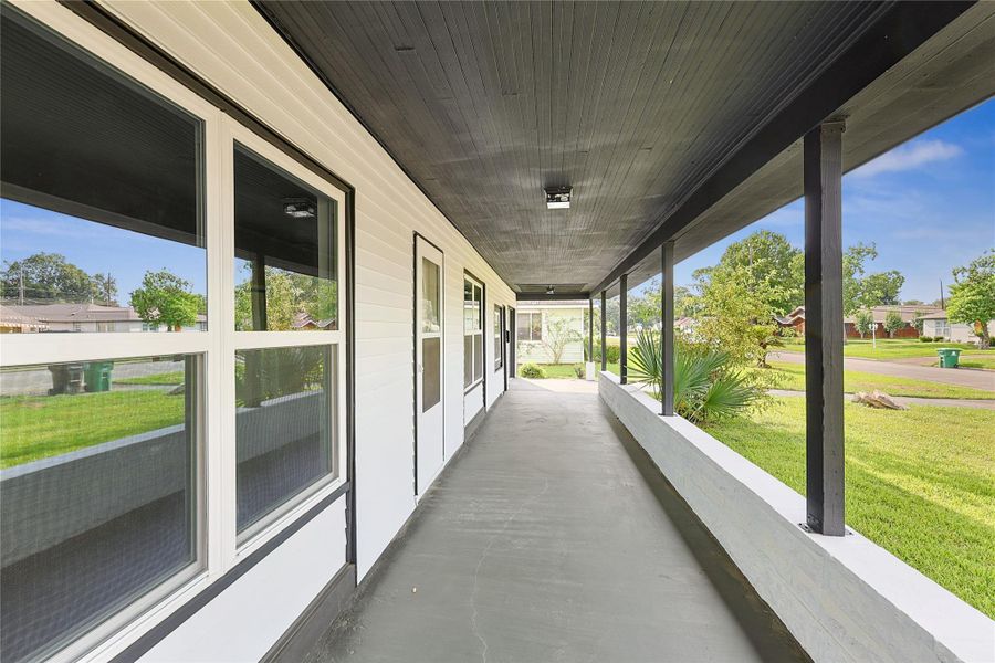 This photo showcases a spacious covered front porch with a modern black and white color scheme. Large windows line the exterior, offering plenty of natural light, while the surrounding greenery provides a pleasant view.
