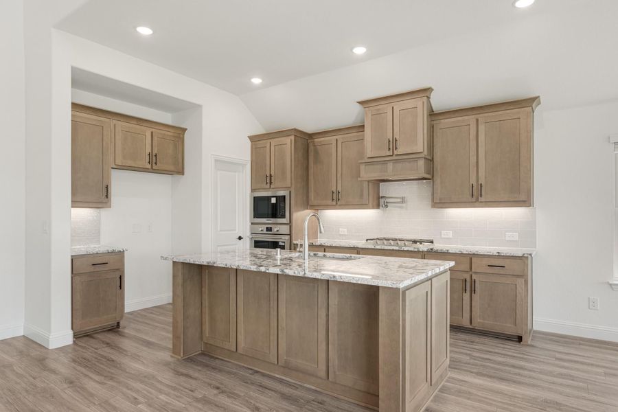 Kitchen with tan wood cabinets, granite island with sink, stainless appliances, and light wood floors Kitchen with tan wood cabinets, granite island with sink, stainless appliances, and light wood floors