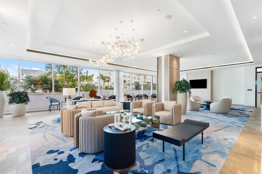 Expansive living space featuring floor-to-ceiling glass windows, recessed tray ceilings, decorative chandelier lighting, wood-finish herringbone flooring, and built-in wall paneling