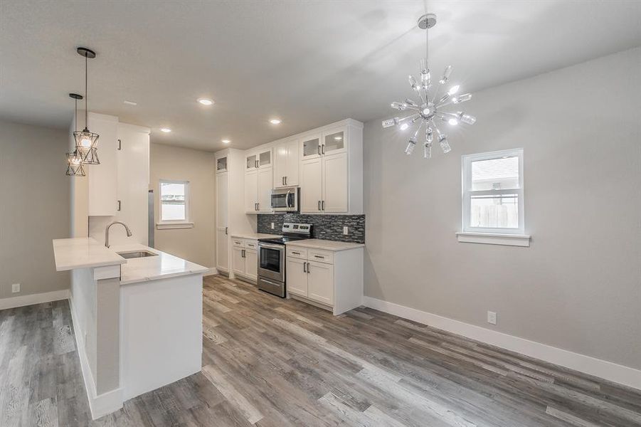 Kitchen featuring white cabinetry, stainless steel appliances, hardwood / wood-style flooring, kitchen peninsula, and sink