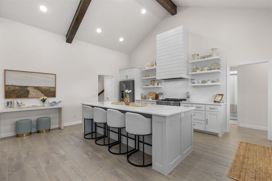 Kitchen featuring white cabinetry, high vaulted ceiling, a kitchen bar, tasteful backsplash, and a kitchen island Kitchen featuring white cabinetry, high vaulted ceiling, a kitchen bar, tasteful backsplash, and a kitchen island