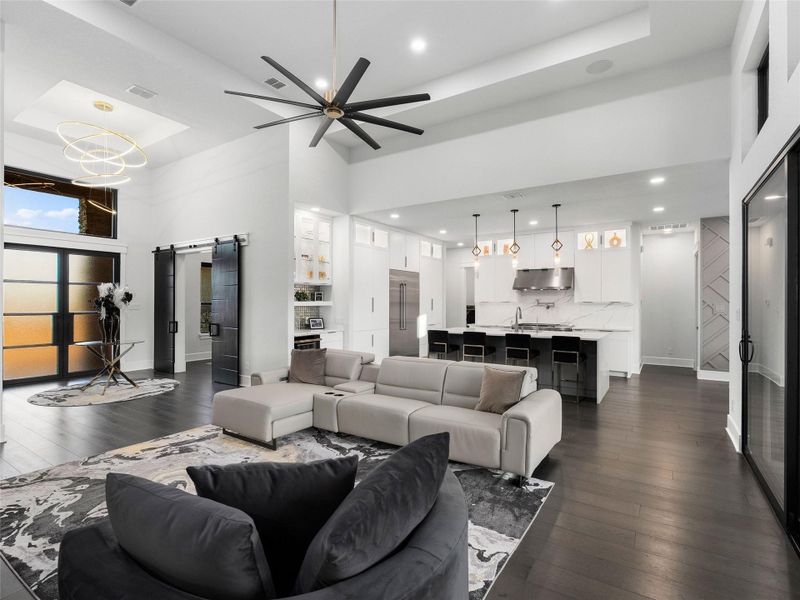 Living area with a barn door, a raised ceiling, dark wood-style flooring, a ceiling fan, and hanging lights