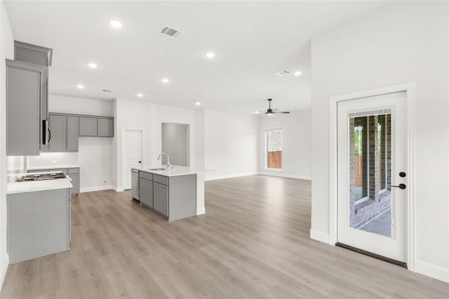 Open-concept kitchen with gray cabinets, center island with sink, and light wood floors leading to living area Open-concept kitchen with gray cabinets, center island with sink, and light wood floors leading to living area