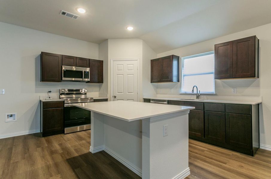 Kitchen featuring stainless steel appliances, light countertops, dark brown cabinets, visible vents, and a sink