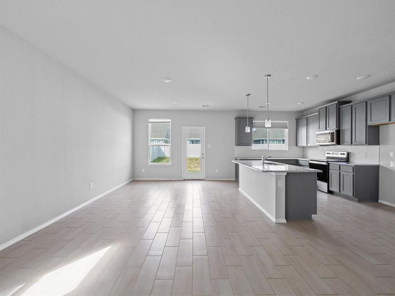 Kitchen featuring an island with sink, stainless steel appliances, hanging light fixtures, open floor plan, and light stone countertops Kitchen featuring an island with sink, stainless steel appliances, hanging light fixtures, open floor plan, and light stone countertops