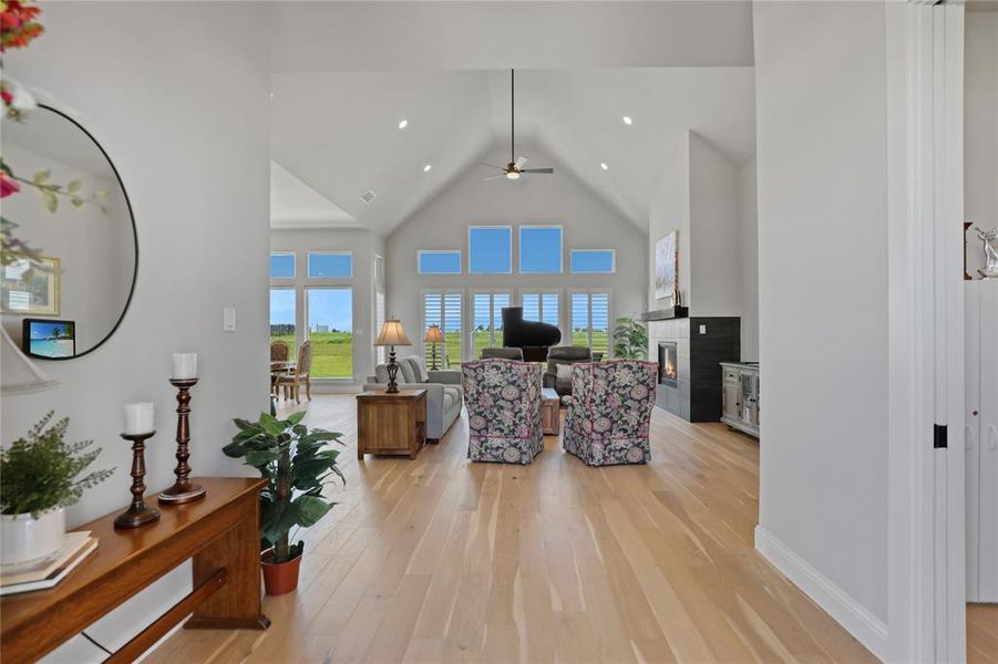Living room with high vaulted ceiling, light wood-type flooring, ceiling fan, a glass covered fireplace, and recessed lighting Living room with high vaulted ceiling, light wood-type flooring, ceiling fan, a glass covered fireplace, and recessed lighting