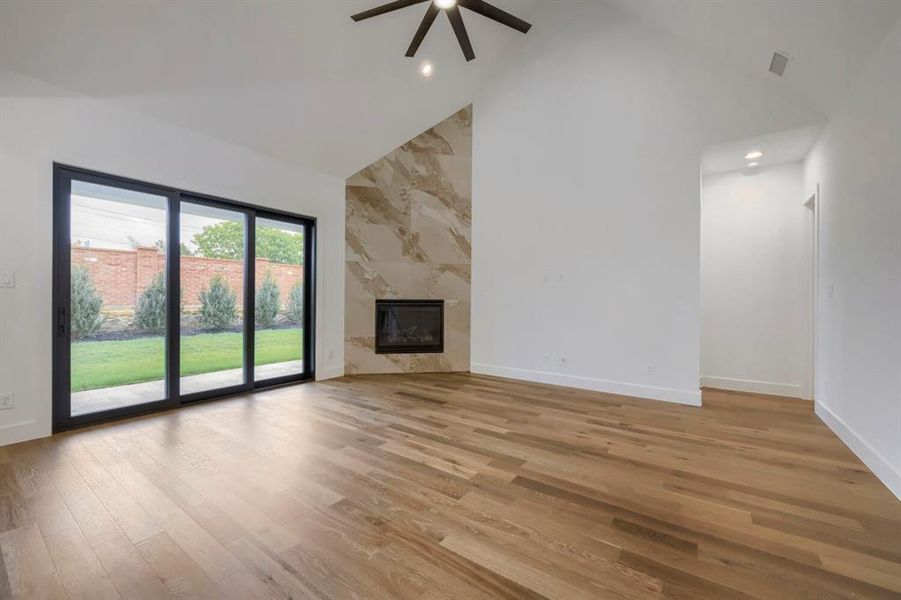 Living area featuring vaulted ceilings, a modern fireplace with a tiled surround, hardwood floors, and large sliding glass doors providing views of the backyard