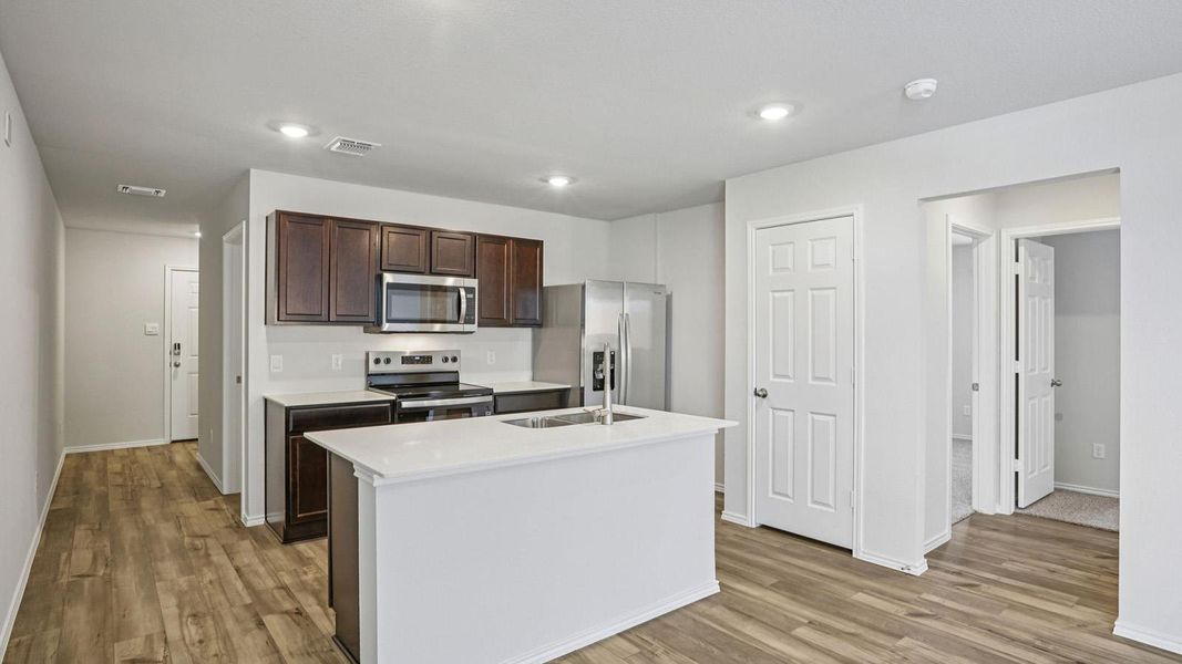 Kitchen featuring stainless steel appliances, a kitchen island with sink, light wood finished floors, dark wood finish cabinets, and recessed lighting