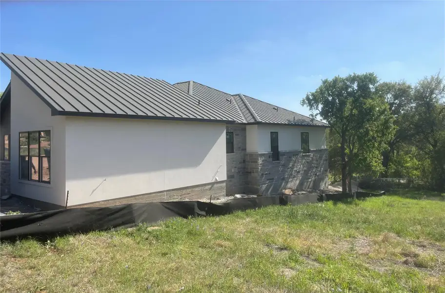 View of property exterior with stucco siding, a standing seam roof, a yard, and stone siding