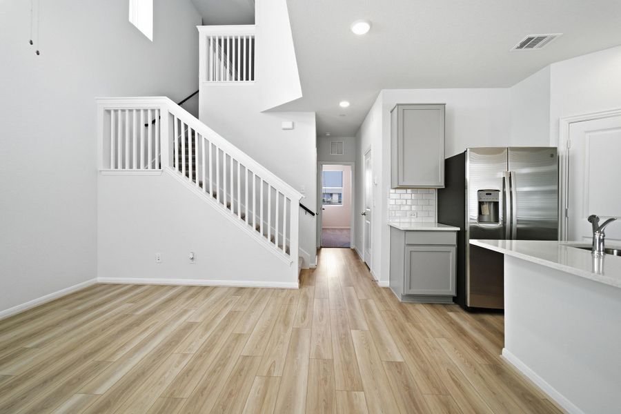 Kitchen with gray cabinets, stainless steel fridge, light wood-style flooring, light stone counters, and tasteful backsplash