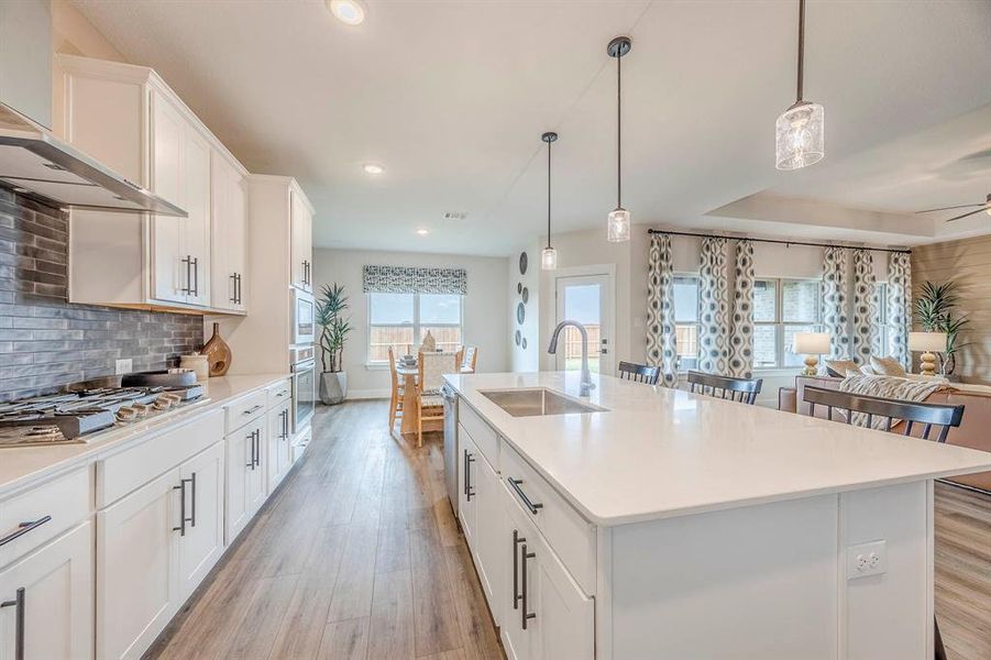 Kitchen featuring white cabinetry, sink, wall chimney range hood, and a healthy amount of sunlight