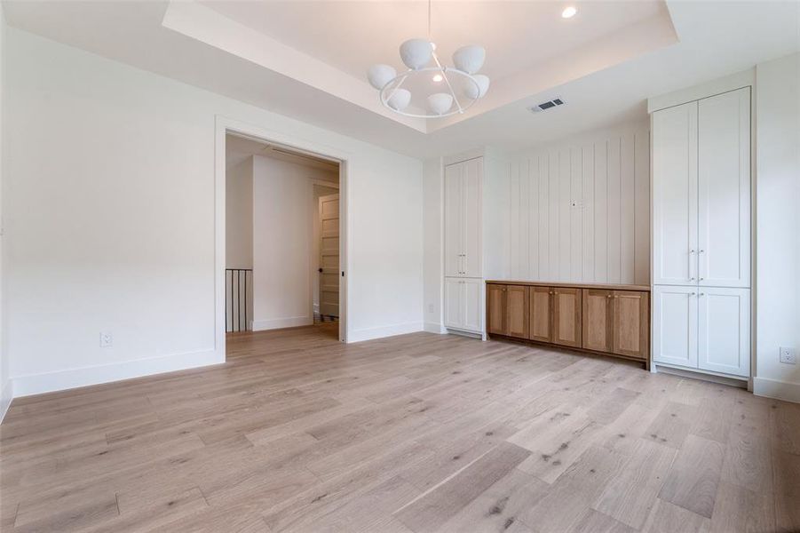 Unfurnished bedroom with a chandelier, a raised ceiling, baseboards, and light wood-style flooring Unfurnished bedroom with a chandelier, a raised ceiling, baseboards, and light wood-style flooring