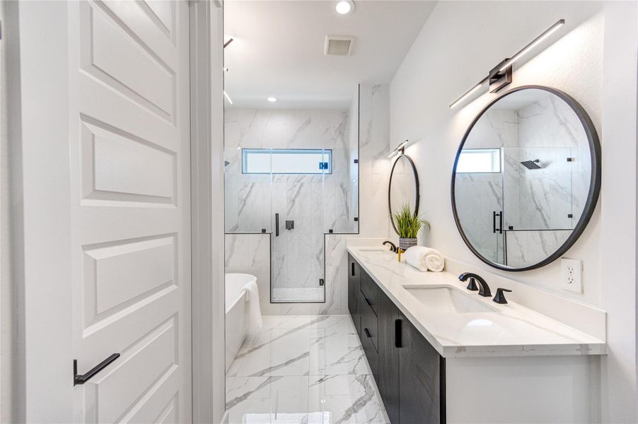 Primary bathroom featuring double vanity sinks with quartz countertops, adjustable anti-fog mirrors, and tile flooring. Highlights include 10-ft ceilings, a freestanding soaking tub, chandelier accent lighting, and a frameless shower with floor-to-ceiling tile.