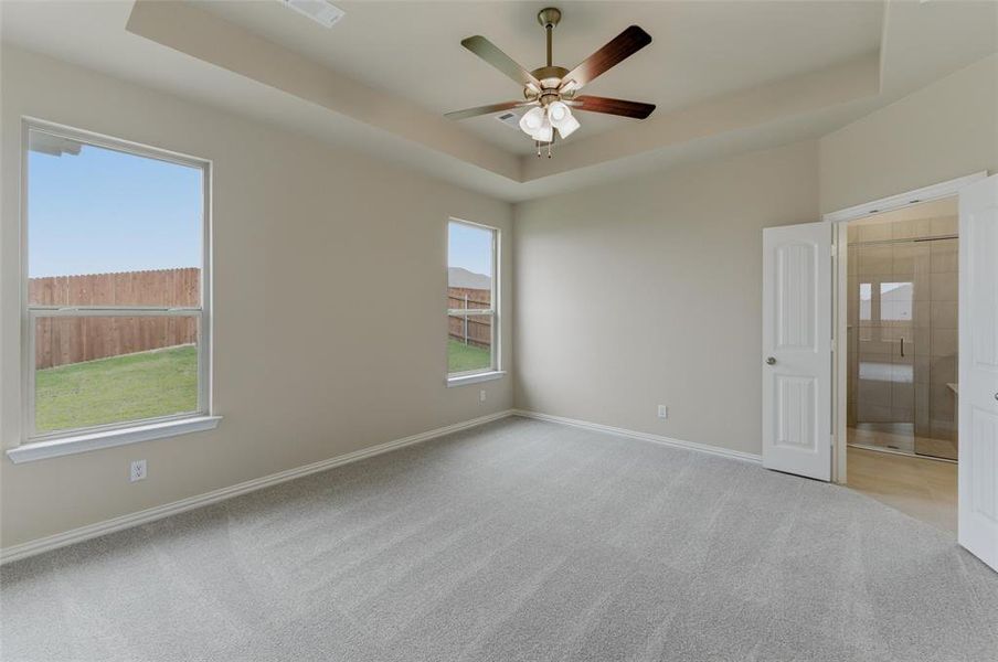 Spacious interior room featuring a tray ceiling with a ceiling fan, carpet flooring, and dual windows