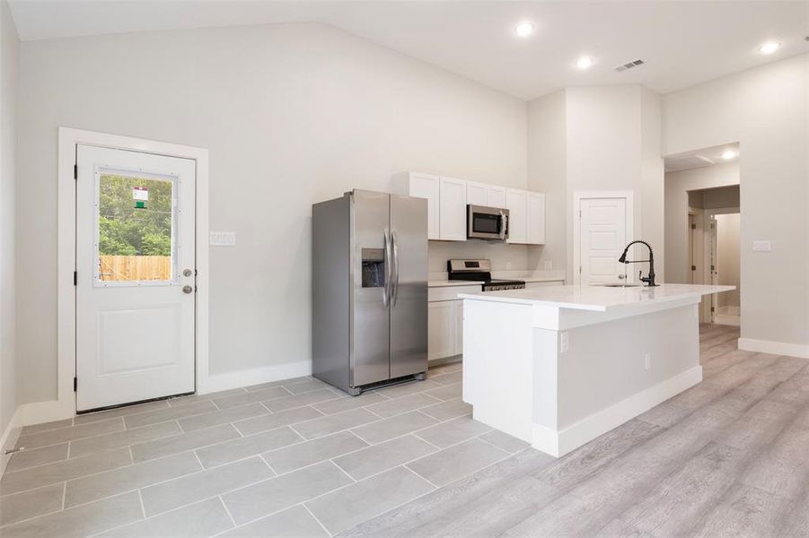 Kitchen featuring white cabinets, stainless steel appliances, a center island with sink, light wood-type flooring, and sink