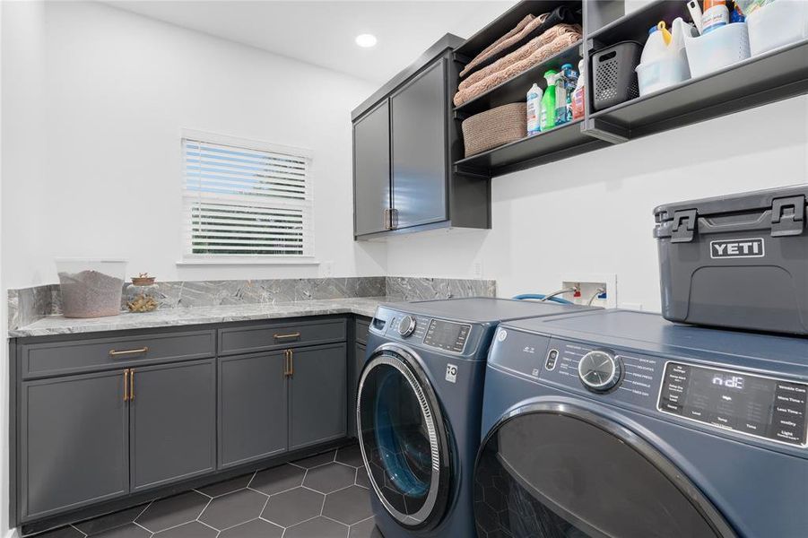 Laundry room featuring hexagon tile flooring, grey cabinetry with gold-tone hardware, grey marble-look countertops, and built-in upper shelving