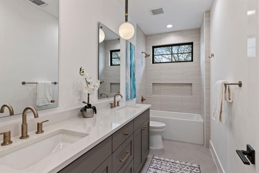 Bathroom with double vanity, toilet, baseboards, and shower / tub combination