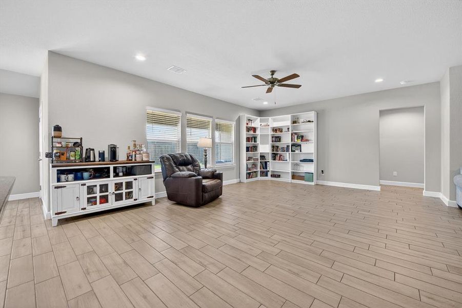 Spacious living area featuring light wood-finish tile flooring, recessed lighting, and a ceiling fan