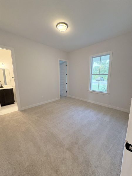Neutral-toned wall-to-wall carpeting, white walls, flush-mounted ceiling light fixture, and a window with white trim Neutral-toned wall-to-wall carpeting, white walls, flush-mounted ceiling light fixture, and a window with white trim