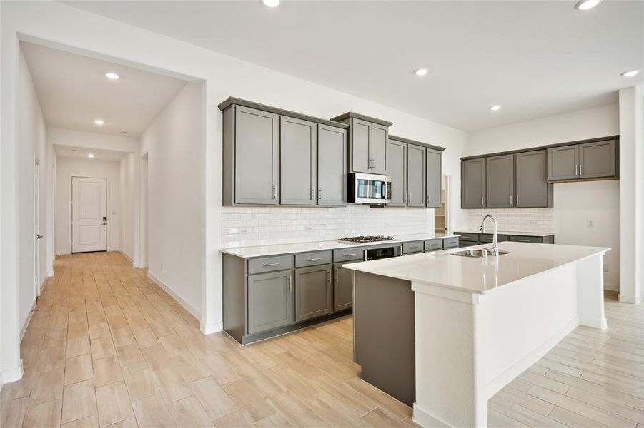 Kitchen with gray cabinetry, sink, stainless steel appliances, and an island with sink