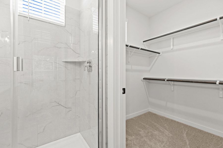 A well-appointed shower featuring elegant tile work adjoins a generously sized walk-in closet with ample shelving. A well-appointed shower featuring elegant tile work adjoins a generously sized walk-in closet with ample shelving.