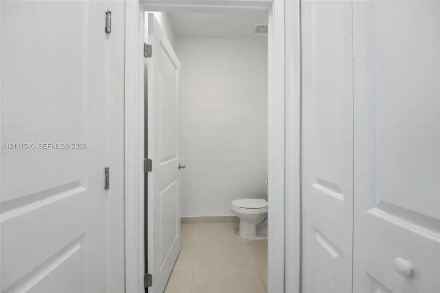 Neutral interior featuring white two-panel doors, neutral large-format floor tile, and a porcelain toilet