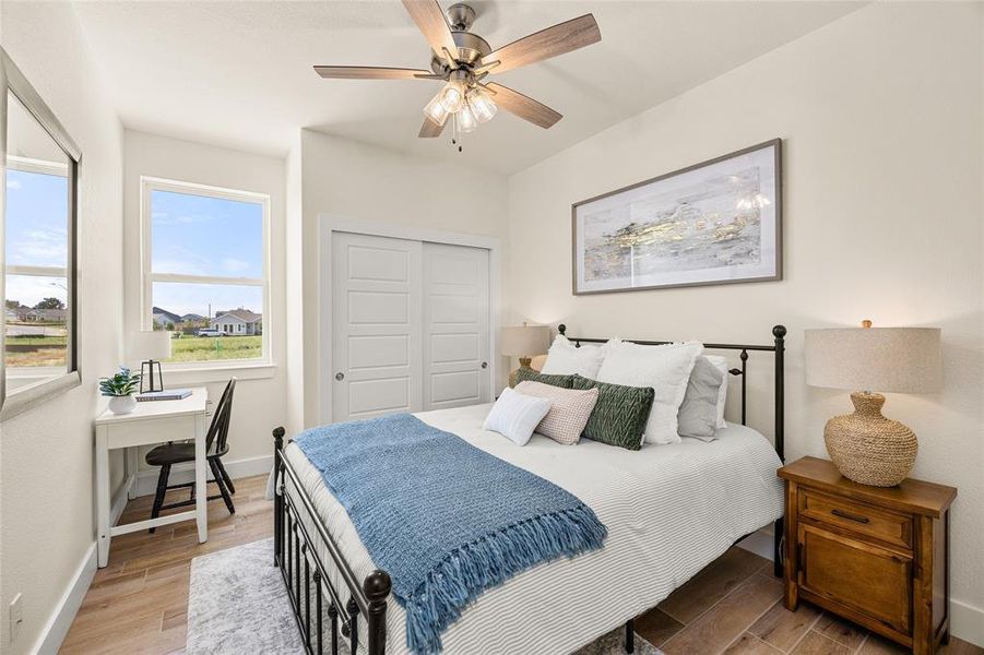 Bedroom featuring light-toned walls, wood-finish flooring, and a ceiling fan with integrated lighting