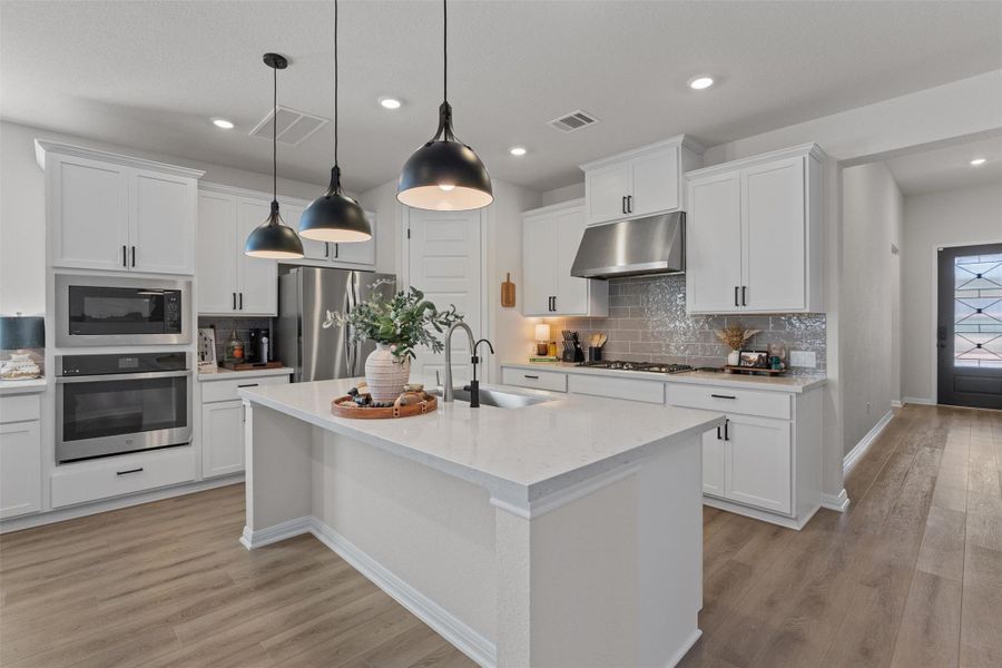 Kitchen with stainless steel appliances, white cabinetry, a center island with sink, light wood finished floors, and light stone counters