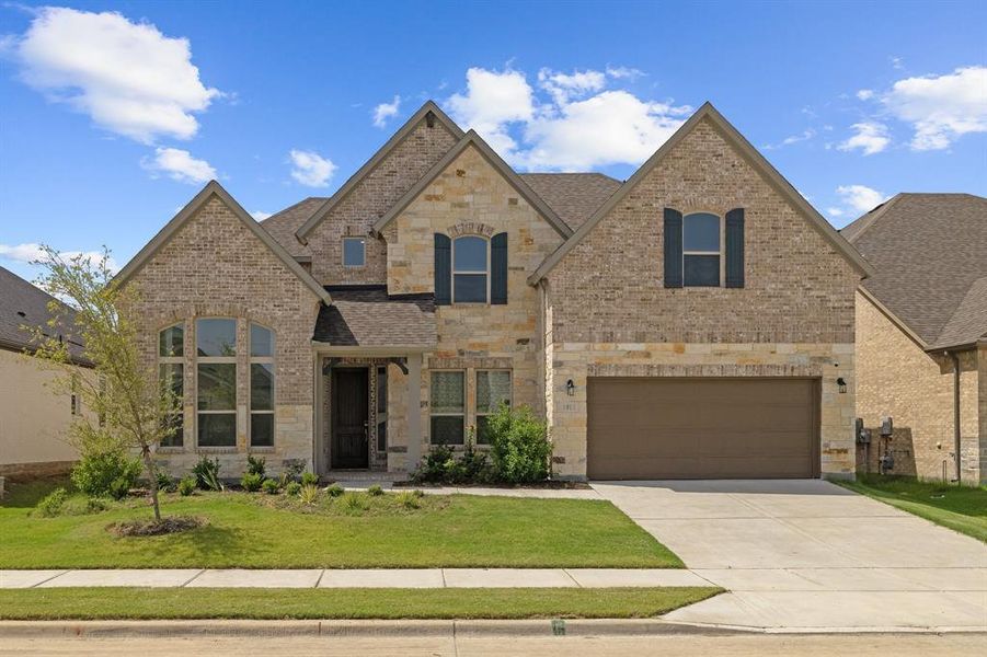 French country style house featuring a shingled roof, concrete driveway, stone siding, a front lawn, and brick siding