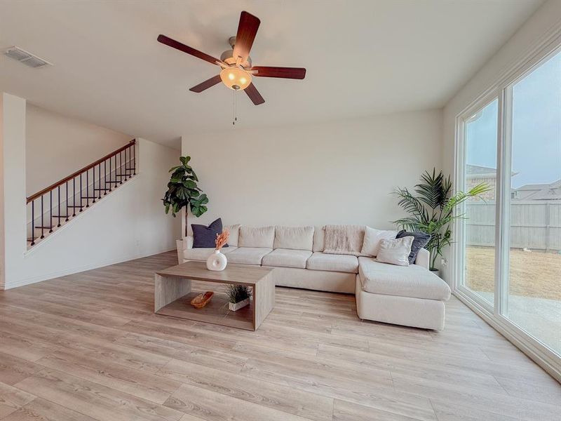 Living room featuring stairs, light wood-type flooring, visible vents, and a ceiling fan