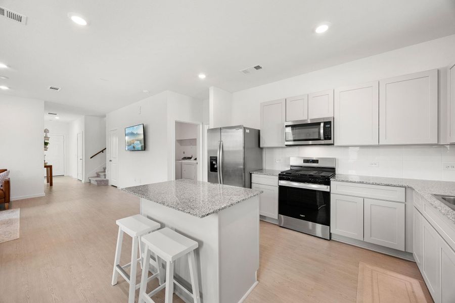 The spacious island provides additional seating and workspace, while the double sink, subway tile backsplash, and abundant cabinetry make daily tasks a breeze. As an added bonus, the refrigerator stays with the home.