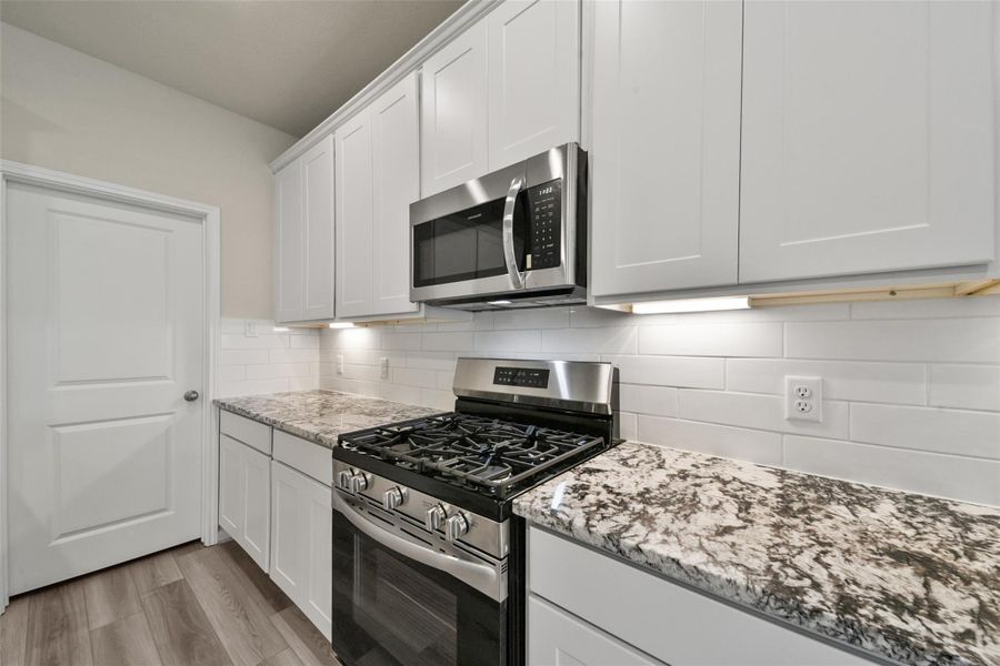 Modern kitchen featuring white cabinetry, granite countertops, and stainless appliances with a classic subway tile backsplash.