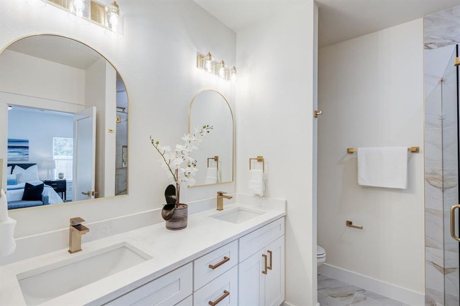 Bathroom featuring tile floors, toilet, double sink vanity, and a shower with shower door