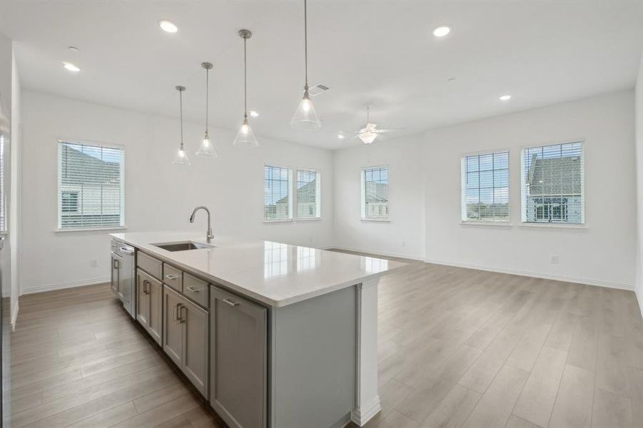 Kitchen with decorative light fixtures, an island with sink, ceiling fan, and sink