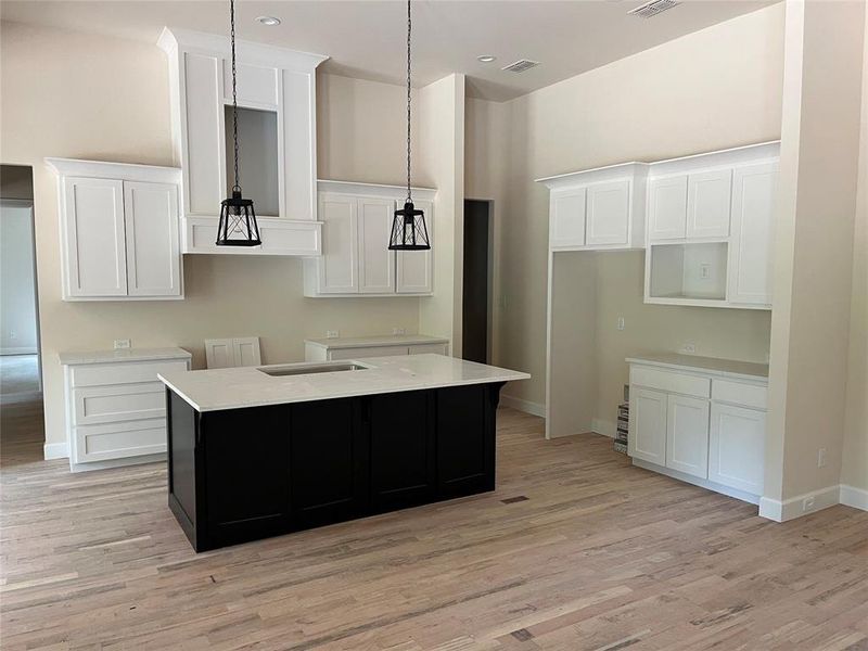 Kitchen featuring custom wood cabinets, a center island with sink and breakfast bar, hardwood flooring, and pendant lighting. Will have Stainless steel gas range, vent hood, microwave, dishwasher. Kitchen featuring custom wood cabinets, a center island with sink and breakfast bar, hardwood flooring, and pendant lighting. Will have Stainless steel gas range, vent hood, microwave, dishwasher.