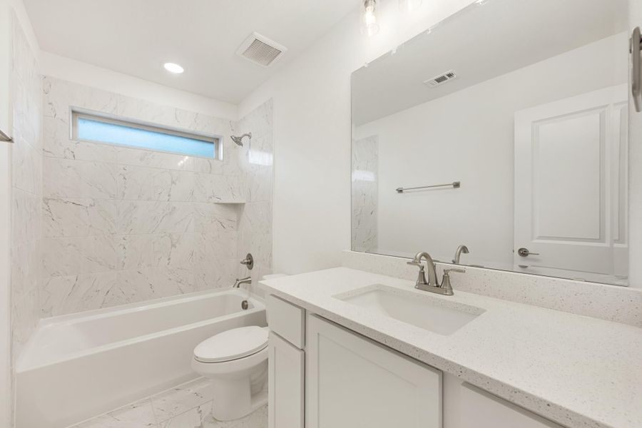 Bathroom with marble tile tub surround, white vanity with quartz countertop, and large mirror