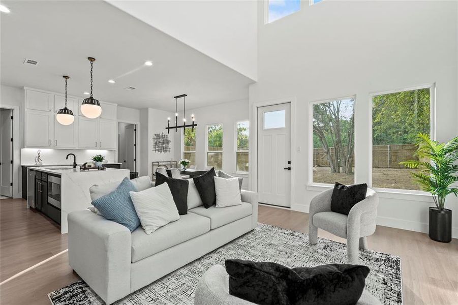 Living room featuring light wood-type flooring, a towering ceiling, recessed lighting, and a chandelier