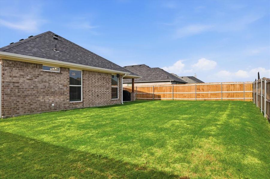 Fenced grassy backyard offering plenty of space for outdoor activities, pets, and entertaining.