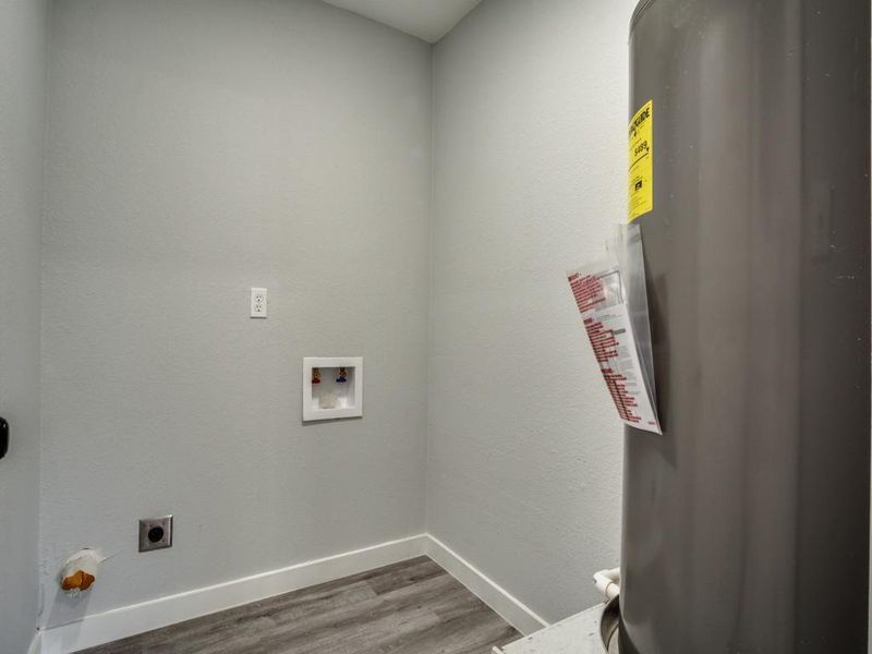 Clothes washing area featuring water heater, hookup for an electric dryer, wood-type flooring, and washer hookup Clothes washing area featuring water heater, hookup for an electric dryer, wood-type flooring, and washer hookup