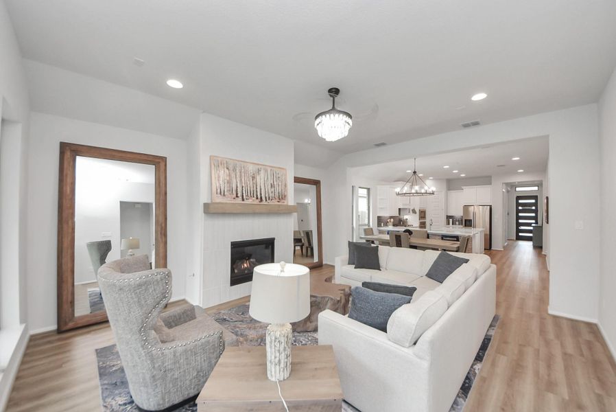 This spacious, open-concept living area features a modern kitchen with stainless steel appliances, a cozy fireplace, and elegant light fixtures. The room is bright and inviting, with a large mirror and stylish furnishings, perfect for family gatherings and entertaining.