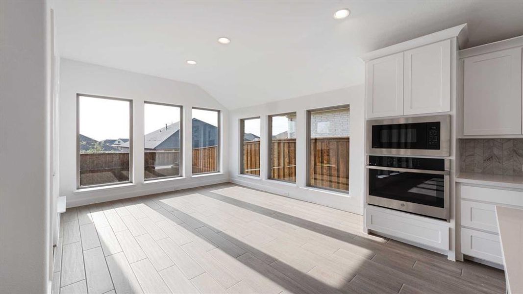 Kitchen featuring light hardwood / wood-style flooring, backsplash, black microwave, vaulted ceiling, and oven