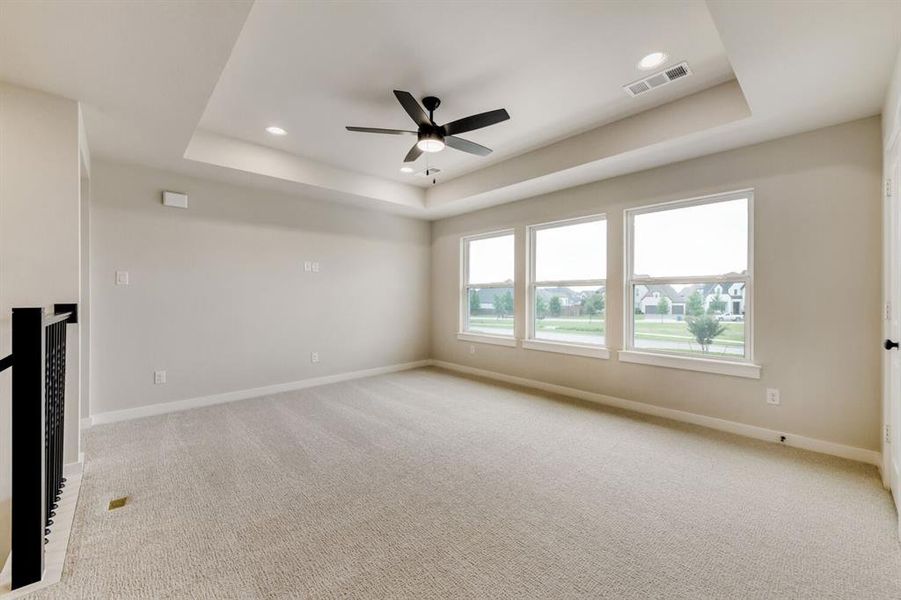 Spacious room featuring light-colored carpeting, a tray ceiling with recessed lighting, and a ceiling fan