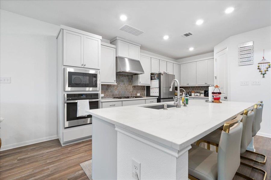 Kitchen with stainless steel appliances, a breakfast bar area, an island with sink, light stone countertops, and tasteful backsplash